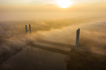 Aerial view of a bridge with cars in the fog. Warsaw. Poland. Drone shot at the traffic of a vehicle traveling in traffic jam on a bridge over a river. Drone shot into the fog at sunrise over a bridg
