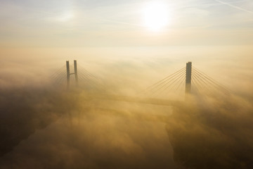Fototapeta premium Aerial view of morning traffic over a bridge Siekierkowski, with dense fog at sunrise. Warsaw. Poland. Drone flies along a low fog bridge at sunrise.
