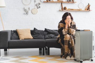 Obraz premium cold girl covering her face while warming up with blanket and heater in living room