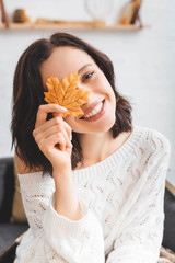 beautiful happy girl holding yellow autumn leaf in front of face