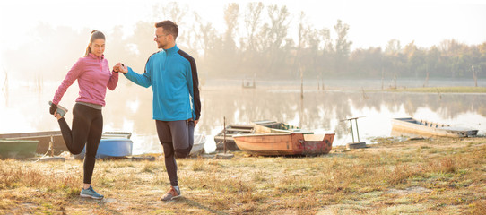 Wide aspect ratio photo of beautiful young couple exercising and stretching by the river or lake....