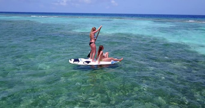 Two girls floating with a surf board over corals and algae on crystal seawater in Australia