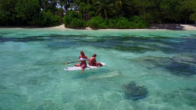Two girls learning to float a surfboard on crystal emerald water of lagoon near exotic island in Jamaica