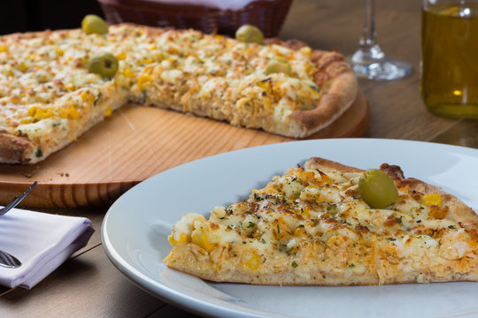 Delicious Catupiry Chicken flavored Pizza served on a wooden board. Made with Mozzarella, Chicken, Creamy Curd, Green Olives, Corn and Red Tomato Sauce. Pizza slice served on the plate.
