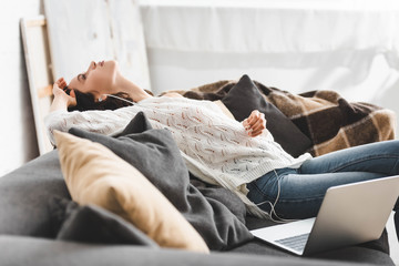 tired girl lying on sofa with earphones and laptop