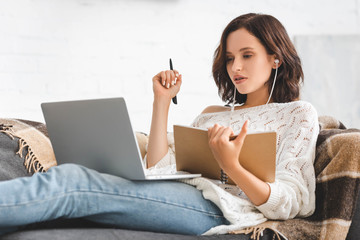 attractive girl studying online with notepad, earphones and laptop