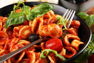 Pasta orecchiette. Plate of delicious orecchiette with tomato sauce garnished with parmesan cheese and basil on rustic background