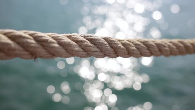 Closeup view of thick rope isolated at blue blurry sunny sparkling sea water background. Real time full hd video footage.