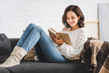 smiling girl reading book on sofa at home