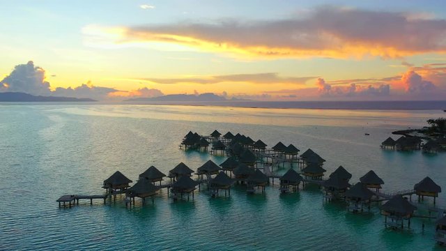 Aerial of charming overwater bungalows on a beautiful tropical beach at sunset, drone flying forward then tilting down over the bungalows and ascending - Bora Bora, French Polynesia