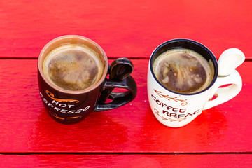 Two cups of homemade expresso coffee on red wooden board.