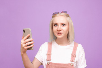 Fototapeta na wymiar Emotional girl with a smartphone in her hands on a purple background looks at the camera with astonishment. Closeup portrait of a surprised teenage girl with a smartphone in his hand. Isolated.