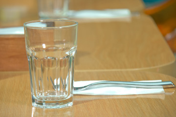 glass on top of wooden table with blurry restaurant . Empty glass on the wooden table in cafe. close up .