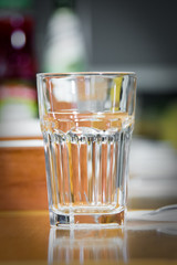 glass on top of wooden table with blurry restaurant . Empty glass on the wooden table in cafe. close up .