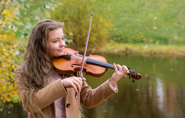Girl playing the violin and smiling in the autumn park at a lake background.