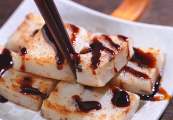 Pouring black soy sauce on ready-to-eat delicious turnip cake, Chinese traditional local dish radish cake in restaurant, close up, copy space.