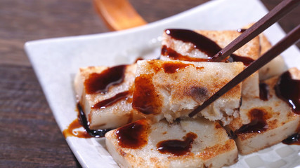 Pouring black soy sauce on ready-to-eat delicious turnip cake, Chinese traditional local dish...
