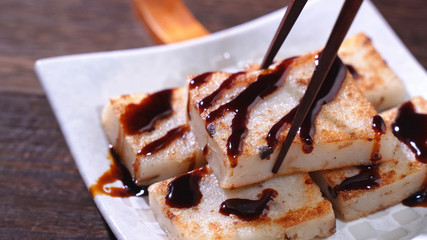Pouring black soy sauce on ready-to-eat delicious turnip cake, Chinese traditional local dish radish cake in restaurant, close up, copy space.