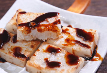 Pouring black soy sauce on ready-to-eat delicious turnip cake, Chinese traditional local dish radish cake in restaurant, close up, copy space.