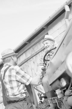 Black and white photo of Senior farmer sitting in tractor while shaking hands with mature farmer 