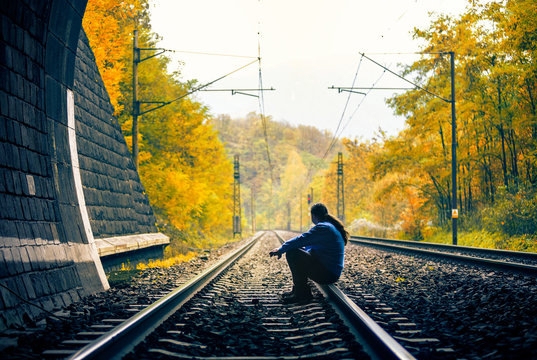 Urbexer sitting on the railway track in the end of the tunnel. Autumn nature in background
