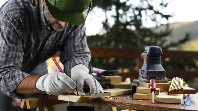 Adult carpenter craftsman wearing helmet and leather protective gloves, with a pencil and the carpenter's square trace the cutting line on a wooden table. Construction industry, housework do it yourse