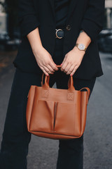 street style portrait of an attractive woman wearing black denim jeans, satin top, blazer, gold watch and holding a tan tote bag, crossing the street. fashion outfit perfect for autumn 2019