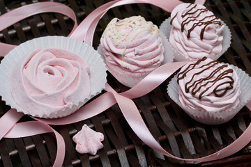 Aerial pink cherry marshmallows. Some in the shape of a rose, another decorated with chocolate. Against the background of wicker vines.