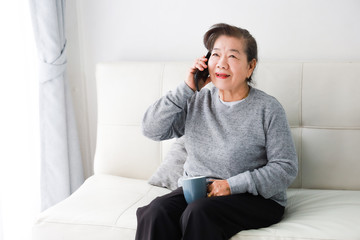 Asian senior woman mother talking with mobile  phone and drinking coffee in living room