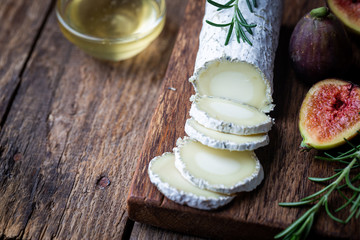 Fresh goat brie cheese with white mold on cutting board, wooden background