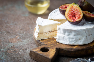 Fresh goat brie cheese with white mold on cutting board, wooden background