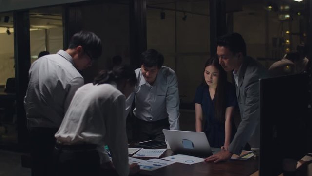 Millennial Asia businessmen and businesswomen meeting brainstorming ideas about new paperwork project colleagues working together planning success strategy enjoy teamwork in small modern night office.
