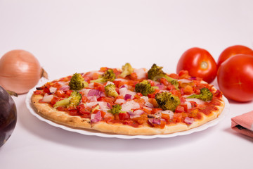 Pizza vegana con tomate, brócoli, cebolla y berenjena sobre fondo blanco.