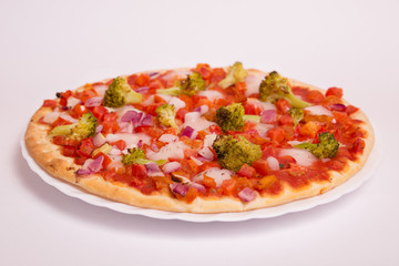 Pizza vegana con tomate, brócoli, cebolla y berenjena sobre fondo blanco.