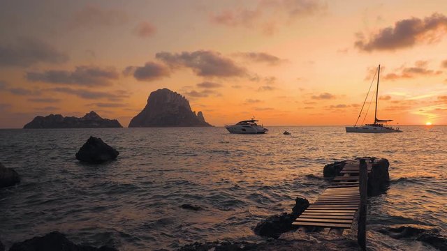 Beautiful seascape at sunset from an old wooden jetty overlooking the Es Vedra islets,and Cala d'hort beach, Ibiza, Spain, with the gentle movement of the water as the sun sets in the orange sky