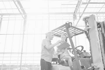 Black and white photo of senior farmer instructing young female farmer driving forklift in greenhouse