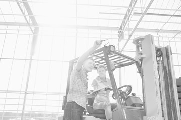 Black and white photo of senior farmer instructing young female farmer driving forklift in greenhouse