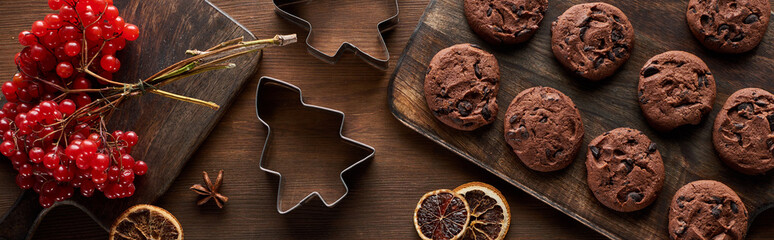 top view of chocolate cookies near Christmas dough molds, viburnum and spices on wooden table, panoramic shot