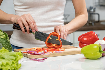 Close up of woman's hands cooking in the kitchen. Housewife slicing fresh Bell pepper. Vegetarian and healthily cooking concept