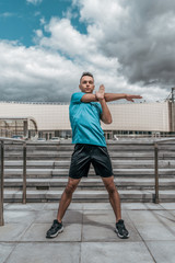 Athletic man, summer afternoon training in city, active lifestyle, modern fitness workout, sportswear t-shirt shorts sneakers. Warming up the muscles before training.