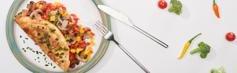 top view of plate with wrapped omelet with vegetables on white table with chili peppers, tomatoes and broccoli