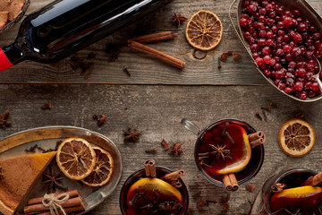 top view of piece of pie, bottle and red spiced mulled wine with berries, anise, orange slices and cinnamon on wooden rustic table