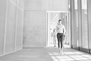 Fototapeta na wymiar Black and white photo of businesswoman using smartphone while walking in office hall