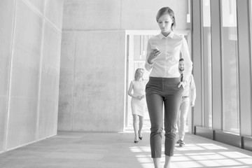 Black and white photo of businesswoman using smartphone while walking in office hall