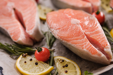 Raw, fresh salmon steaks on a baking tray with lemon, rosemary and cherry tomatoes. Raw salmon, red fish. Cooking salmon, seafood. Healthy eating concept. Salmon and spices