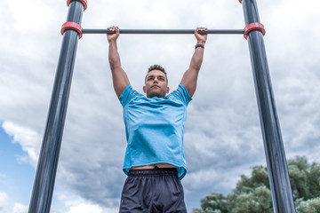 sports man pulls himself up on the horizontal bar, training in city during the summer, an active lifestyle, modern fitness workout.
