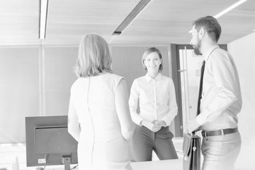 Black and white photo of business people waiting while talking to receptionist in office lobby