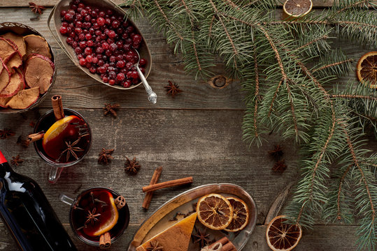 top view of red spiced mulled wine near fir branch, berries, anise, orange slices and cinnamon on wooden rustic table