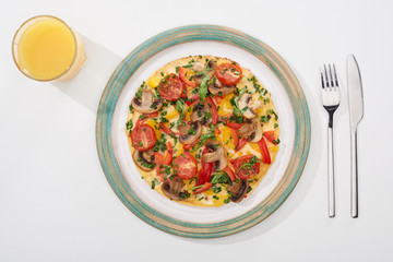top view of plate with homemade omelet for breakfast on white table with glass of juice, fork and knife