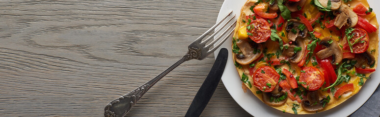 top view of omelet on plate with fork and knife on wooden table